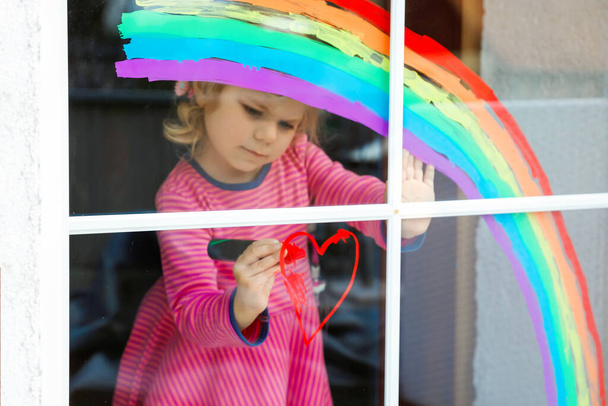 Маленька дівчисько-адоральниця з веселкою забарвлена барвистим віконним кольором під час карантину. Дитина малює веселки по всьому світу зі словами "Давайте все добре".. - Фото, зображення