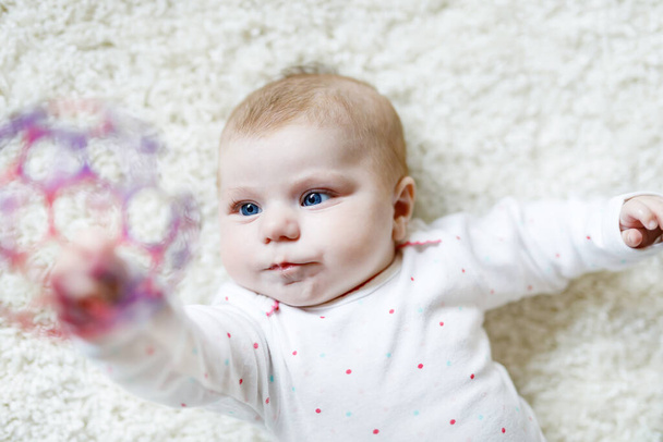 Cute adorable newborn baby playing with colorful ball toy on white background. New born child, little girl looking at camera. Family, new life, childhood, beginning concept. Baby learning grab rattle. - Photo, Image