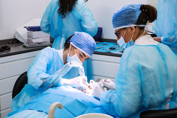 Szakmai női fogorvos és asszisztens orvosi maszkok és sapkák gyógyító fogak a beteg munka közben a modern fogászati klinikán - Fotó, kép