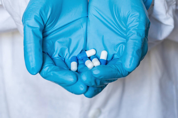 Der Arzt oder Apotheker in blauen Handschuhen mit Kapseln in der Hand - Foto, Bild