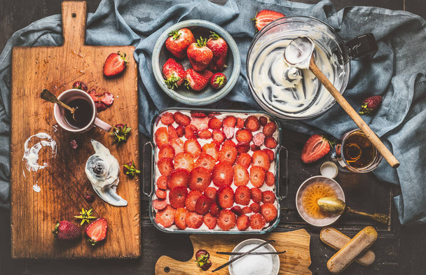 Strawberries cake cooking preparation on rustic kitchen table with kitchen tools and ingredients, top view - Zdjęcie, obraz