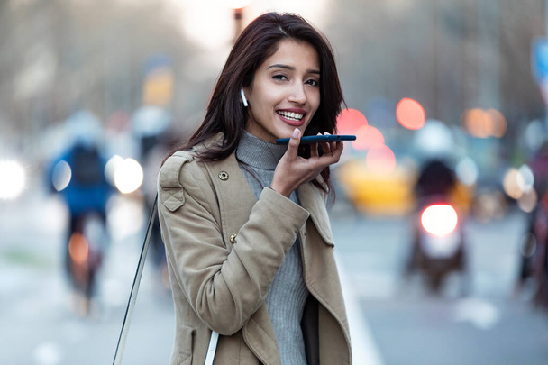 Shot of pretty young woman using voice recognition system on her smartphone while standing in the street. - Foto, Imagem