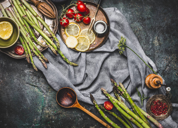 Asparagus with wooden spoon and cooking ingredients, preparation on dark rustic background, top view, frame - Фото, зображення