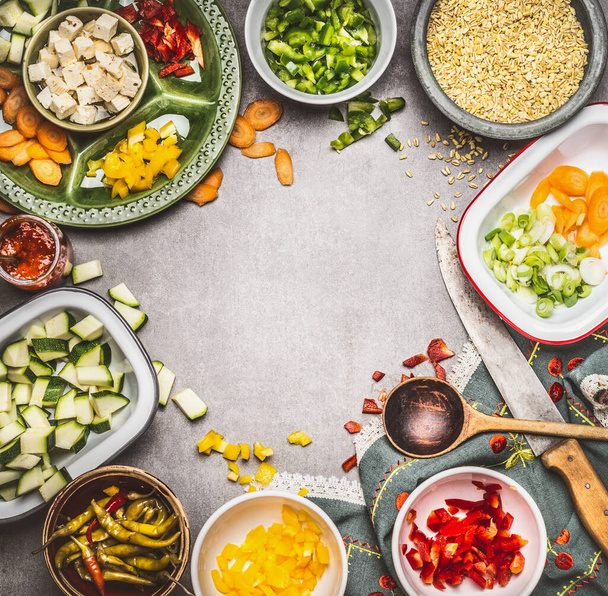 Sağlıklı vejetaryen yemeği hazırlamak için peynir dilimleri, tabakta sebzeler, inci arpa, yemek kaşığı ve mutfak bıçağı, üst manzara. Temiz Beslenme Konsepti - Fotoğraf, Görsel