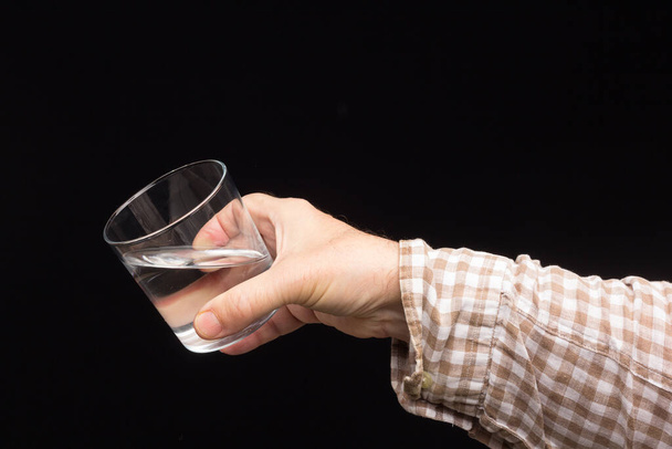 Transparant glazen bekertje in de hand van een persoon. Glas gevuld met water of transparante vloeistof. Drinkwater - Foto, afbeelding