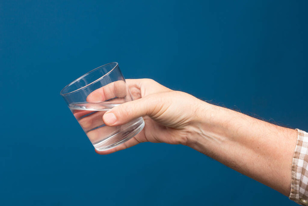 Διαφανές γυάλινο κύπελλο στο χέρι ενός ατόμου. Γυαλί γεμάτο με νερό ή διαφανές υγρό. Πόσιμο νερό - Φωτογραφία, εικόνα