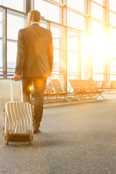 Вид сзади на зрелого бизнесмена, идущего с чемоданом на воротах для посадки в аэропорту
 - Фото, изображение