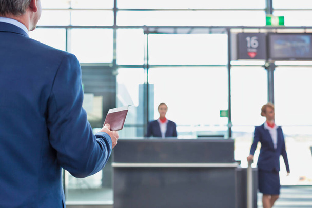 Rear view of mature businessman holding his passport and boarding pass at airport - Valokuva, kuva