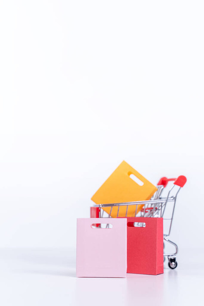 Shopping bags in a silver red shopping cart isolated on white table background, concept of staying home order, close up, copy space design. - Fotografie, Obrázek