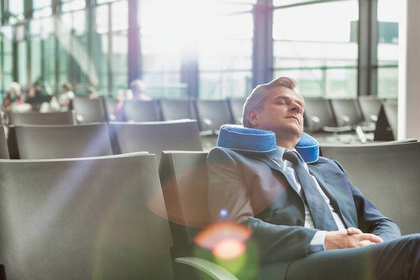 Mature businessman sitting and sleeping with his pillow while waiting for boarding in airport - Foto, imagen