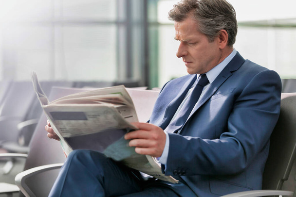 Volwassen zakenman zitten en het lezen van de krant tijdens het wachten op instappen in de luchthaven - Foto, afbeelding
