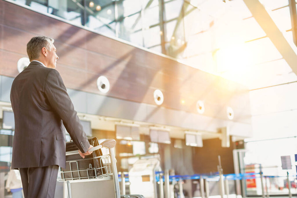 Mature businessman pushing baggage cart for check in at airport - Foto, imagen
