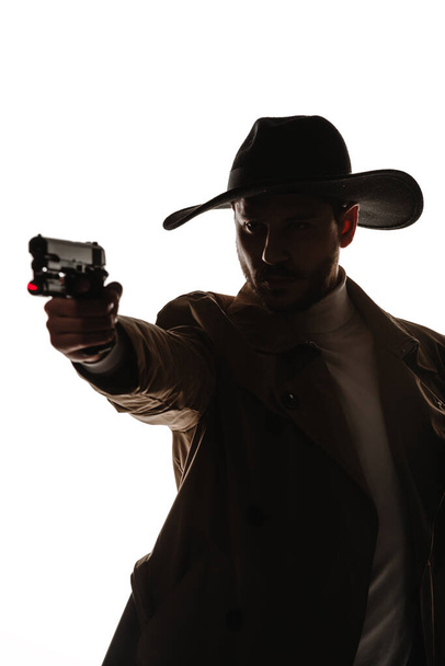 Atraktivní mladý muž pózující v futuristickém detektivním obleku, držící v ruce pistoli - Fotografie, Obrázek