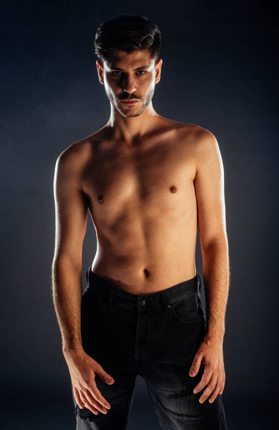Приваблива молода чоловіча модель позує топлес в рваних чорних джинсах
 - Фото, зображення