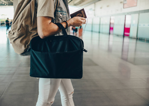 Молодой человек, стоящий с чемоданом и паспортом в зале ожидания в аэропорту
 - Фото, изображение