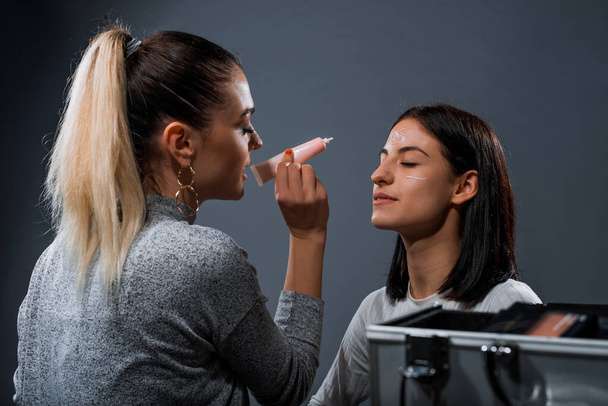 Make-up kunstenaar het aanbrengen van crème op een aantrekkelijke vrouwelijke model - Foto, afbeelding