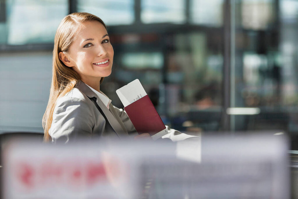 Portrait of young attractive businesswoman holding her passport and boarding pass in airport - Фото, изображение