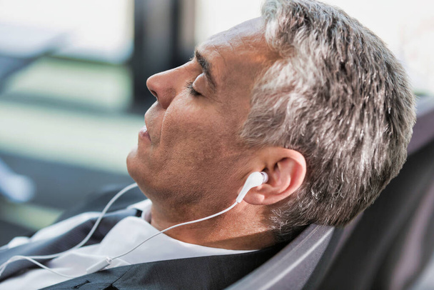Portrait of mature businessman listening to music on his smartphone while sleeping and waiting for boarding in airport - Foto, Bild