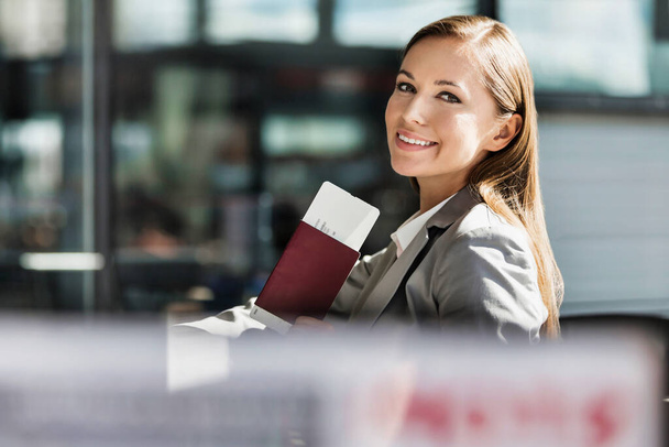 Portrait of young attractive businesswoman holding her passport and boarding pass in airport - Foto, Imagen