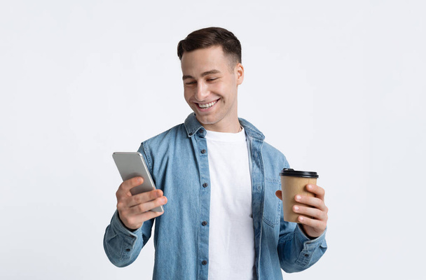 Cup and smartphone in hands of guy - Photo, image