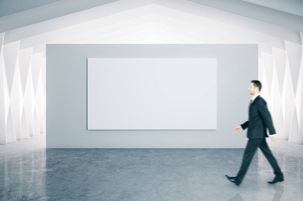 Geschäftsmann zu Fuß und leeres Plakat im modernen Galerieinterieur. Kunst und Design-Konzept. - Foto, Bild