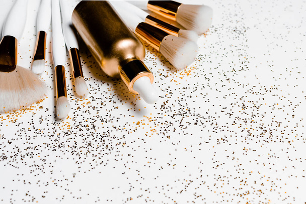 Makeup brushes, hyaluronic acid and golden glitter confetti on white background. Top horizontal view copyspace. - Photo, Image
