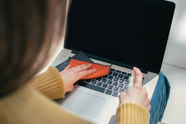 de près. une jeune femme utilise un antiseptique pour nettoyer son ordinateur portable - Photo, image
