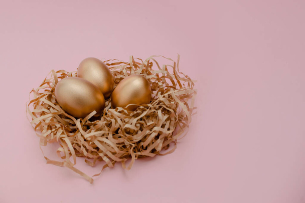Easter golden decorated eggs in nest on pink background . Minimal easter concept copy space for text. Top horizontal view, flatlay. - Photo, Image