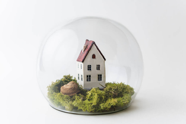 Conceptual image of safety when staying at home during Corona virus COVID-19 quarantine lockdown. Small toy house under the glass with moss and grass around. - Photo, Image