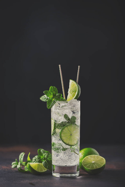 Alcoholic mojito with lime, mint  and ice on the black background, selective focus and toned image - Fotografie, Obrázek