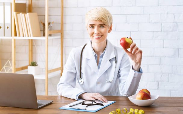 Médico en la oficina a la mesa con manzana en las manos
 - Foto, Imagen