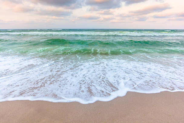 χρυσαφί συννεφιασμένο ηλιοβασίλεμα πάνω από τα πράσινα νερά. κύματα συντρίβουν την αμμώδη παραλία. Καθαρό ορίζοντα. αλλαγή θυελλώδους καιρού - Φωτογραφία, εικόνα