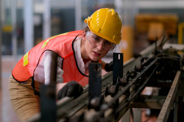 Όμορφη εργάτης ή τεχνικός γυναίκα κοιτάξουμε μπροστά μέσω της σιδηροτροχιάς κάποιου μηχανήματος στο εργοστάσιο εργασίας. - Φωτογραφία, εικόνα