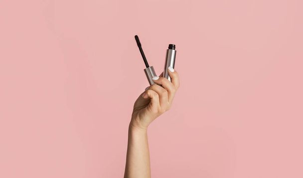 Beauty and makeup. Young girl holding mascara on pink background, close up - Foto, Imagen