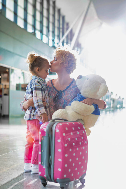 Portrait of mother reuniting and kissing her daughter on forehead in airport - 写真・画像