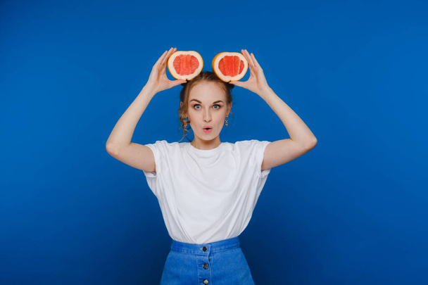 Surprised, the laughing girl holds the grapefruit like ears. Vegan lifestyle. Smiling woman , eating concept.Diet organic , weight loss and healthy food. Smoothies and fresh juice. - Photo, image