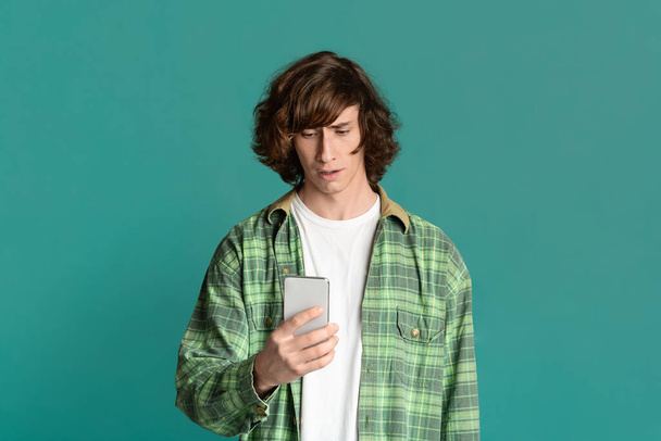Расстроенный молодой парень, использующий смартфон для онлайн-общения, цветной фон
 - Фото, изображение