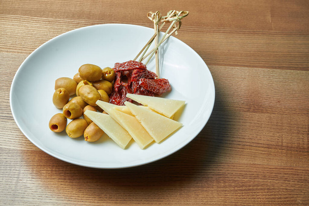 Předkrm italské antipasto - sušená rajčata, olivy a parmezán v bílém talíři na dřevěném podkladu - Fotografie, Obrázek