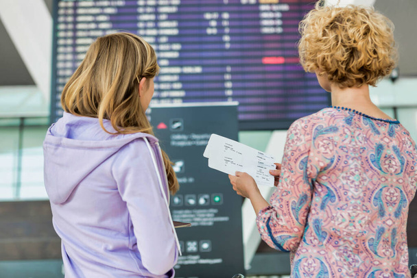 Portrait of mother and daughter looking at flights on monitor in airport - Foto, Imagen