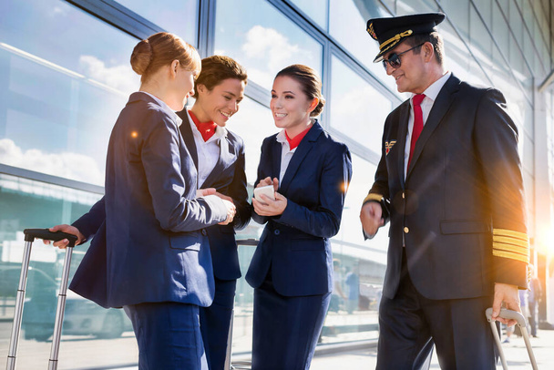 Portrait of mature pilot talking with young attractive flight attendants during arrival in airport - Fotoğraf, Görsel