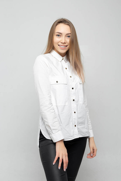 Beautiful young woman portrait. Portrait of a beautiful smiling blonde girl in a white shirt on a white-gray. - Photo, image