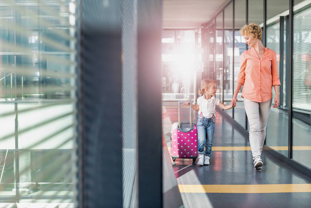 Portrait of mature woman walking with her daughter in arrival area at airport with lens flare - Foto, Imagem