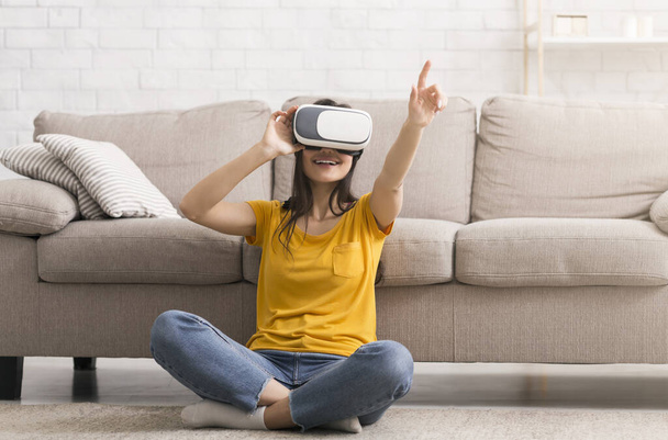 Веселі карантинні хобі. Тисячолітня дівчина в гарнітурі віртуальної реальності грає в онлайн гру вдома
 - Фото, зображення