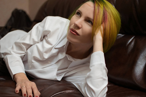 A woman with multi-colored hair is lying on a leather sofa. - Fotoğraf, Görsel