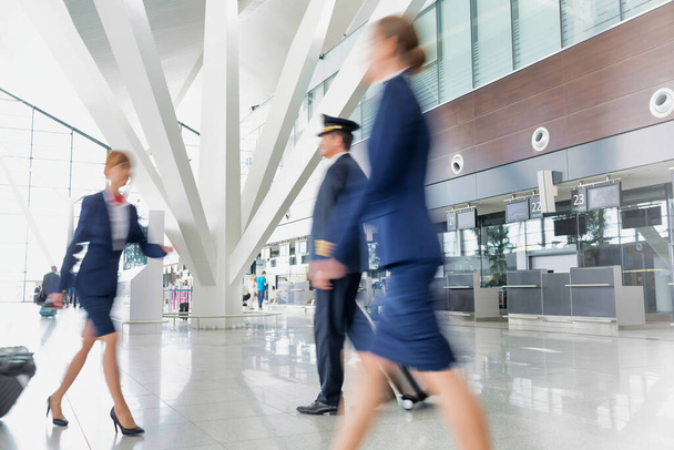 Mature pilot with young beautiful flight attendants walking in airport - Photo, image