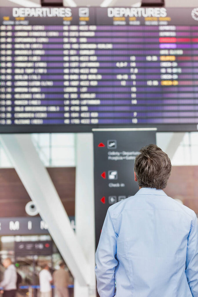 Vista trasera del hombre maduro mirando su posición vertical en la pantalla en el aeropuerto
 - Foto, Imagen