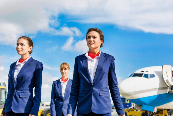 Photo of three confident flight attendants walking against airplane in airport - Фото, зображення