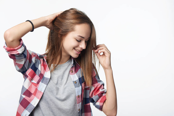 Smiling relaxed teen girl touching her hair looking down, studio portrait - 写真・画像