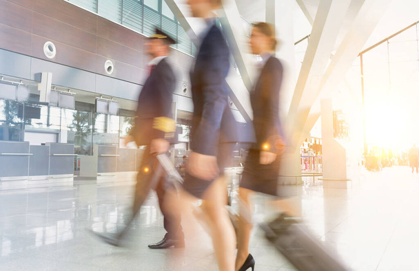 Mature pilot with young beautiful flight attendants walking in airport - 写真・画像