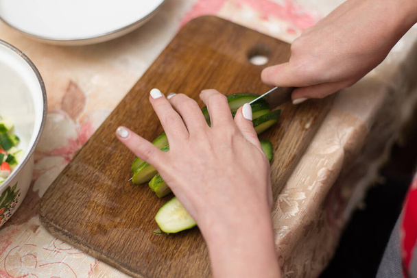 Woman cuts cucumbers on the cutting board. - Фото, зображення